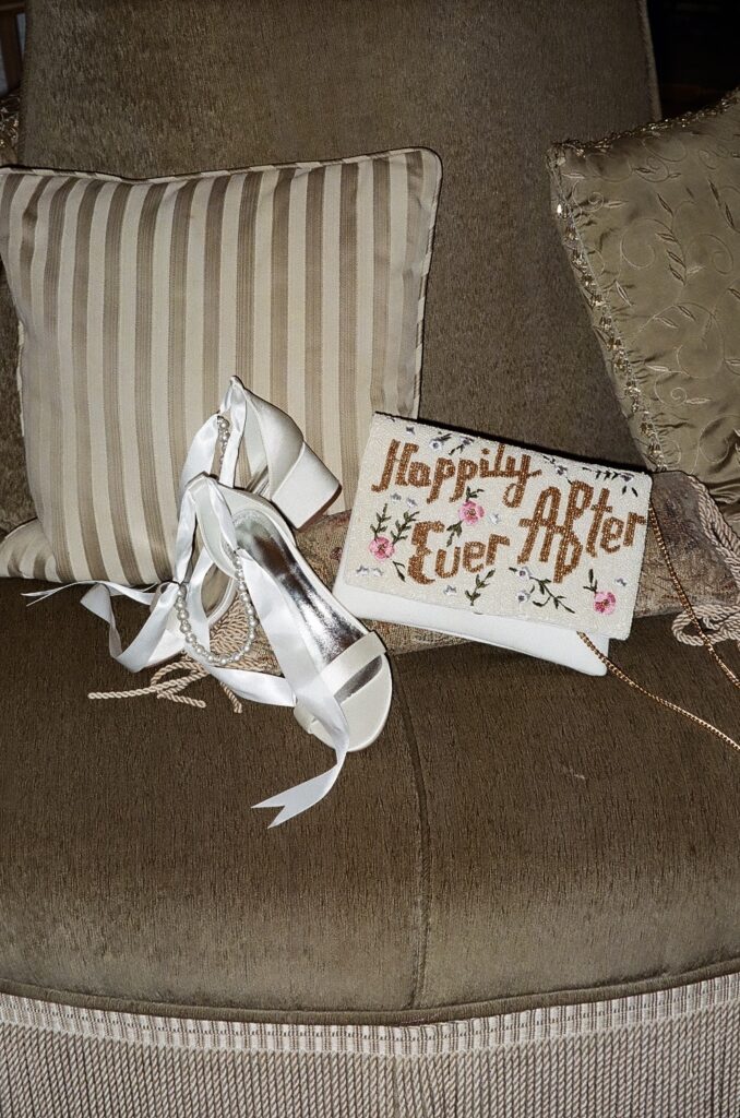 Bridal accessories including pearl heels and a ‘Happily Ever After’ clutch styled on a vintage chair capturing the kind of wedding day details a virtual assistant for wedding vendors can help organize and manage.